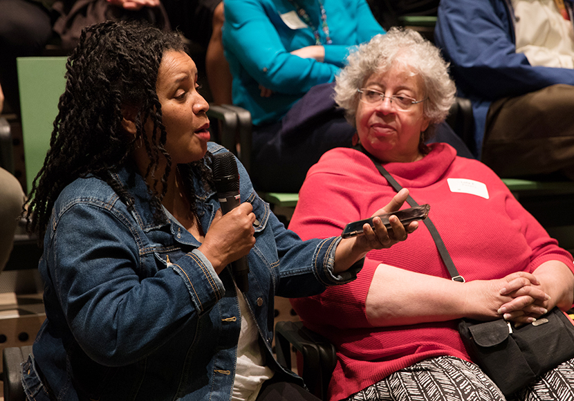 Two adults seated in auditorium seats and having a conversation.