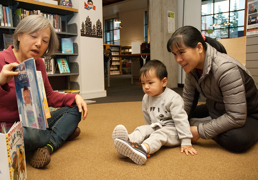 Two adults and one child seated on floor with a book.